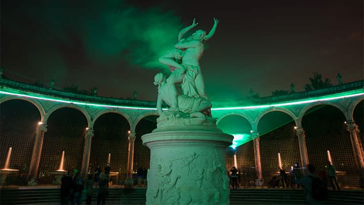 Statue et colonnade éclairées en vert dans les jardins de Versailles la nuit