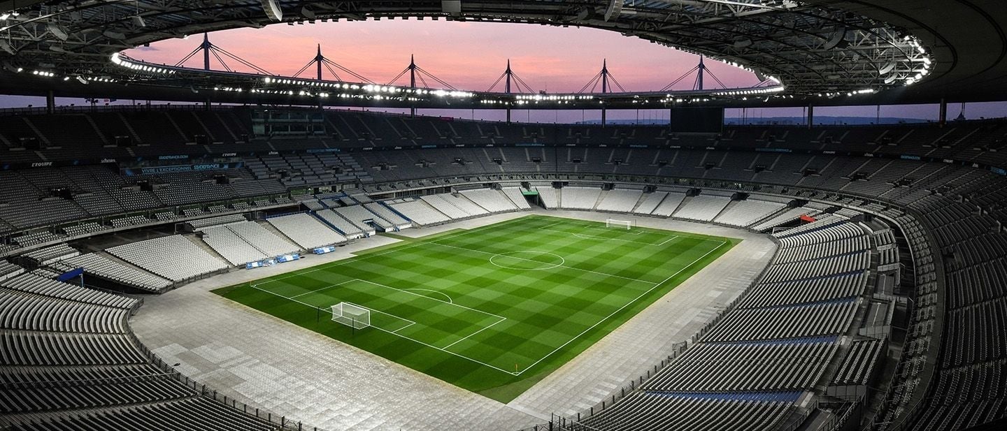 La pelouse et les tribunes sous la toiture en ellipse suspendue aux mâts, au crépuscule